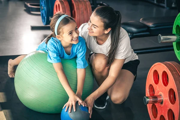 Little sporty girl and young beautiful mother doing stretching with fitness ball at gym.