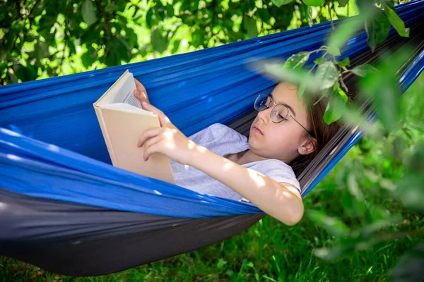 Cute Teen Dziewczyna Okularach Czyta Książkę Leżąc Hamaku Ogrodzie — Zdjęcie stockowe