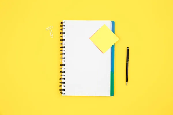 Blank notepad and paper reminder on yellow background, top view, copy space.
