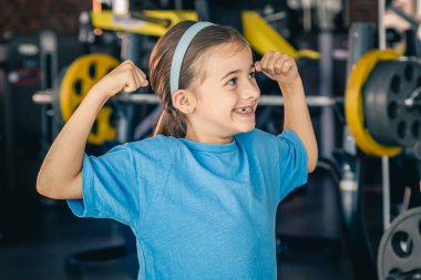 Çekici küçük kız spor yaparken kaslarını gösteriyor ve gülümsüyor..