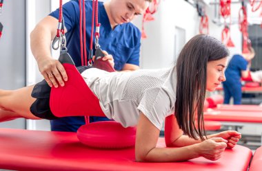 Kayropraktik uzmanı kadın hasta bacağını esnetiyor, erkek fizyoterapist egzersiz odasında kadının bacağını esnetmesine yardım ediyor..