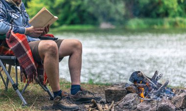 İnsanın arka planda kitap okuduğu şenlik ateşine yakın çekim doğa, açık hava eğlence konsepti, kopyalama alanı.
