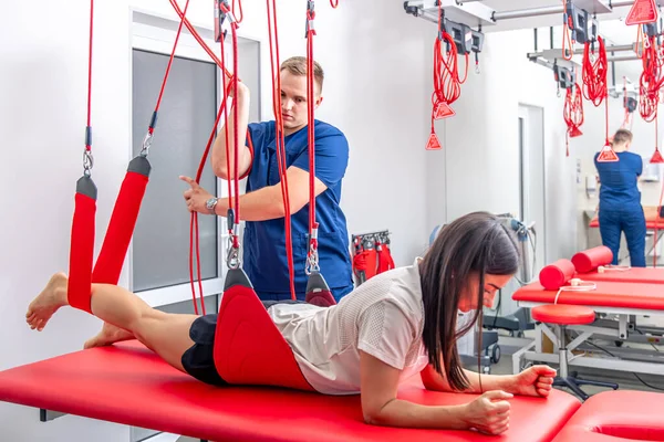 stock image A young woman is doing working out with personal trainer at fitness center, modern rehabilitation physiotherapy male worker with client.