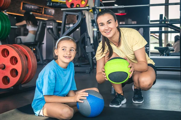 Strong mother with daughter in the gym go in for sports, use balls, happy family.