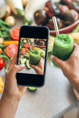 Bir kadın akıllı telefondan sebze kokteylinin fotoğrafını çekiyor, bir blogcu yemeğin fotoğrafını çekiyor, kilo kaybı ve detoks konsepti..