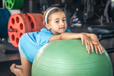 Mutlu kız vücudunu spor salonunda bir fitbol topuna, jimnastiğe ve çocuklar için pilatese dayar..