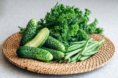 Salatalık, lahana ve yeşil fasulye mutfak masasında hasır bir tabakta..