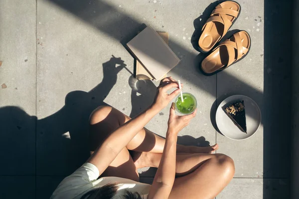 Summer composition with slippers, books, cake and lemonade in female hands, hard shadows on a sunny day, top view.