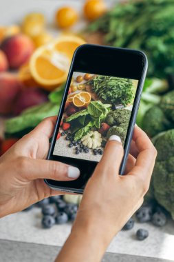 Kadın elleri sebzelerin akıllı telefon fotoğrafları, sosyal medya için telefon fotoğrafçılığı veya blog yazarlığı, sağlıklı beslenme.
