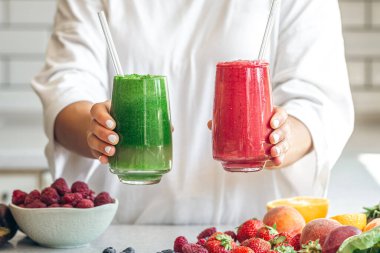 Kadın ellerinde bir bardak kırmızı ve yeşil meyve püresi, yakın plan, sağlıklı beslenme, detoks ve yaz içecekleri..