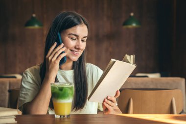 Kafede bir bardak limonatayla kitap okuyan çekici genç bir kadın. Lezzetli bir yaz atıştırmalığı..