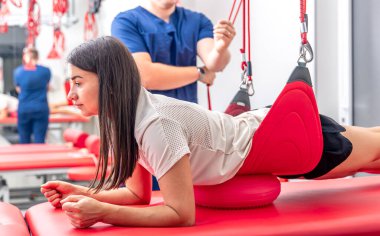 Kayropraktik uzmanı kadın hasta bacağını esnetiyor, erkek fizyoterapist egzersiz odasında kadının bacağını esnetmesine yardım ediyor..