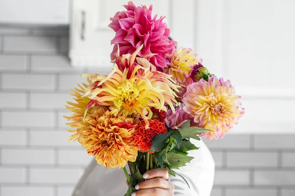 A woman holding a bouquet of yellow and orange dahlias on a white background, the concept of flower workshops and articles for the study of floristry.