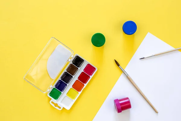Art palette with paint and brushes on a yellow background, workplace for creativity, home teaching concept drawing, back to school concept.