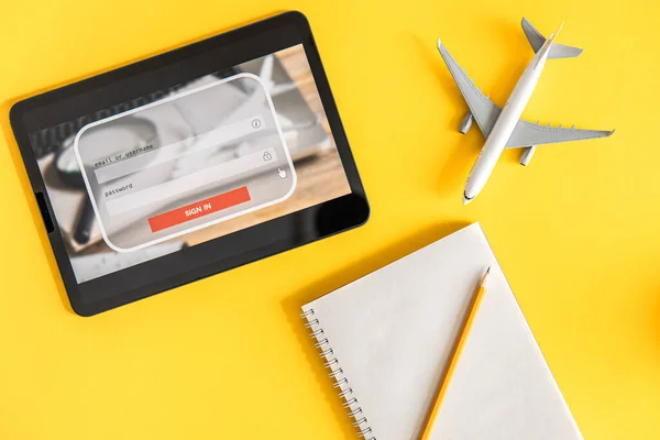 Login box, username and password inputs on virtual digital display, notebook and plane on a yellow background, the concept of travel planning, booking and buying tickets.