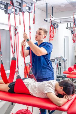 Fizyoterapist, özel bir askıya alma halat sistemi üzerinde rehabilitasyon gören modern bir fitness merkezinde kadın hastaya yardım ediyor..