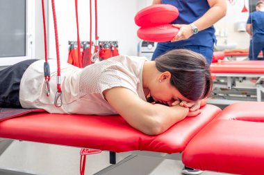 Fizyoterapist, özel bir askıya alma halat sistemi üzerinde rehabilitasyon gören modern bir fitness merkezinde kadın hastaya yardım ediyor..