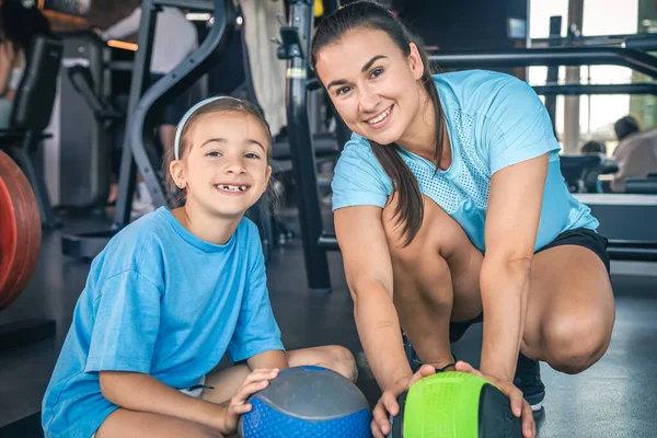 Strong mother with daughter in the gym go in for sports, use balls, happy family.