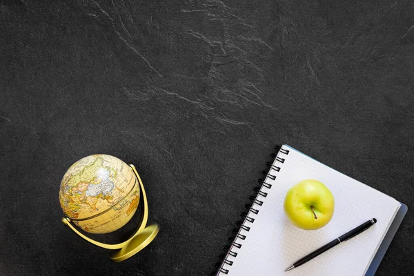 Globe, notepad and apple on black background, top view, school concept, copy space.