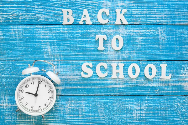 Back to school, banner with the inscription with wooden letters and alarm clock on a blue wooden background, top view.