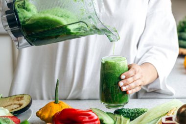 Evde detoks yeşil smoothie yapan bir kadın, cama smoothie döken bir kadın, sağlıklı gıda konsepti..