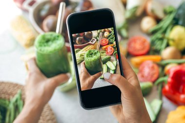 Bir kadın akıllı telefondan sebze kokteylinin fotoğrafını çekiyor, bir blogcu yemeğin fotoğrafını çekiyor, kilo kaybı ve detoks konsepti..
