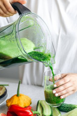 Evde detoks yeşil smoothie yapan bir kadın, cama smoothie döken bir kadın, sağlıklı gıda konsepti..