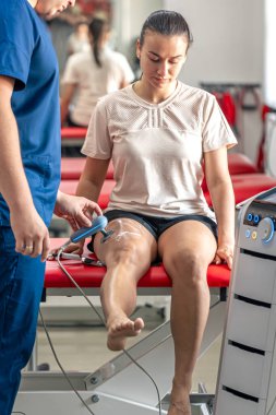 Doktor, T-CaRe teknolojisi, direnç ve kapasite terapisi olan bir hastanın diz eklemlerini tedavi etmek için makine kullanıyor..