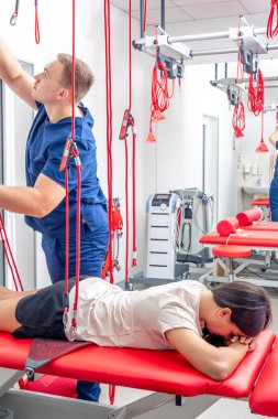 Fizyoterapist, özel bir askıya alma halat sistemi üzerinde rehabilitasyon gören modern bir fitness merkezinde kadın hastaya yardım ediyor..