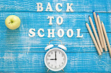 Okula geri dön, üzerinde tahta harfler ve alarm saati olan afiş ve mavi ahşap arka plan, üst görünüm..