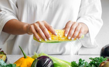 Yakın plan, mısır kadınların elinde ve diğer sebzeler mutfak masasında..