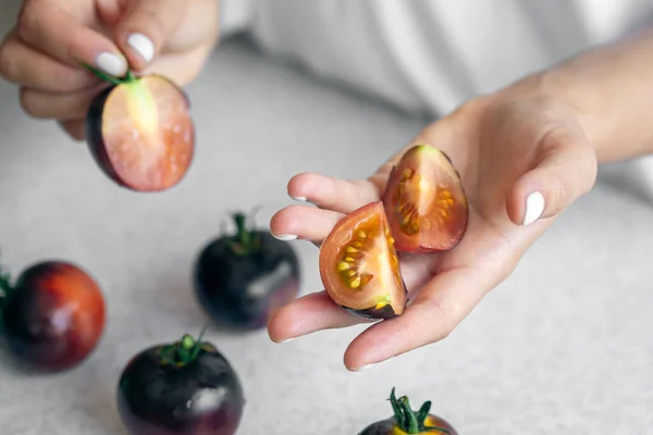 Black tomatoes in female hands close-up against the background of a white kitchen table, cooking in the kitchen.