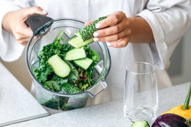 Sağlıklı beslenme, yemek pişirme, vejetaryen yiyecekler, diyet ve insan konsepti, evde detoks veya smoothie için yeşil sebze doğrayan bir kadına yakın çekim.