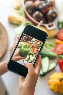 Bir kadın akıllı telefondan sebze kokteylinin fotoğrafını çekiyor, bir blogcu yemeğin fotoğrafını çekiyor, kilo kaybı ve detoks konsepti..