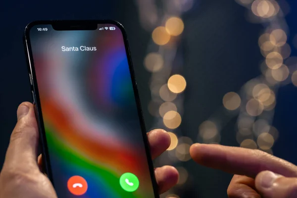 stock image Christmas incoming call from Santa Claus, hand holding smartphone with incoming call screen on a blurred background with bokeh.