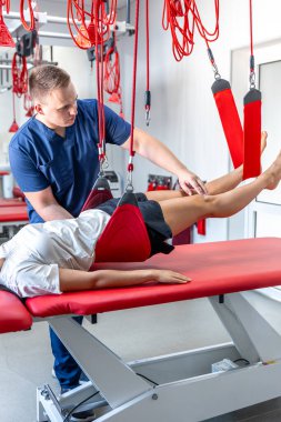 Kadın hastaya süspansiyon kayışları tedavisi uygulayan rehabilitasyon uzmanı, ağrısız dolaşım düzenini iyileştirmek için terapi egzersizleri, nöro-fonksiyon teknikleri..