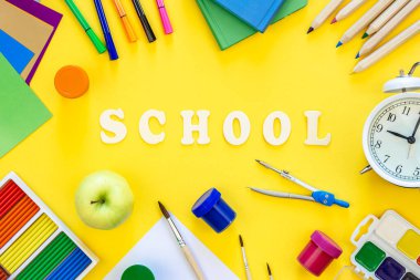 Renkli okul gereçleri ve sarı arka planda ahşap harfler. Okul konseptine geri dönüyoruz..