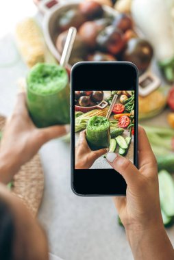 Bir kadın akıllı telefondan sebze kokteylinin fotoğrafını çekiyor, bir blogcu yemeğin fotoğrafını çekiyor, kilo kaybı ve detoks konsepti..
