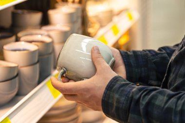 Ev eşyaları dükkanındaki raftan büyük gri bardakları tutan adam..