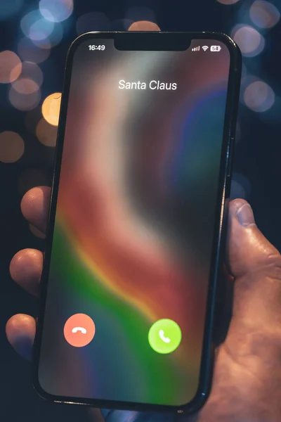 Christmas incoming call from Santa Claus, hand holding smartphone with incoming call screen on a blurred background with bokeh.