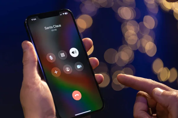 stock image Christmas incoming call from Santa Claus, hand holding smartphone with incoming call screen on a blurred background with bokeh.