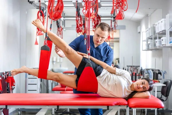 Female patient hanging on suspensions at rehabilitation center, therapeutic exercises and neuromuscular activation on red cord slings, Neurac technique.