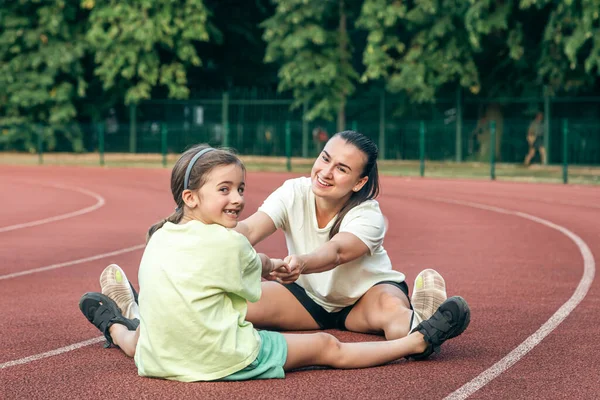 Mother and daughter go in for sports outdoors, caucasian woman and little girl are engaged in fitness at the stadium.