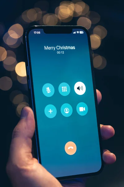 Incoming call screen from Merry Christmas in hands on a dark blurred background with bokeh.