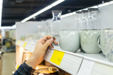 Ev eşyaları dükkanındaki raftan büyük gri bardakları tutan adam..
