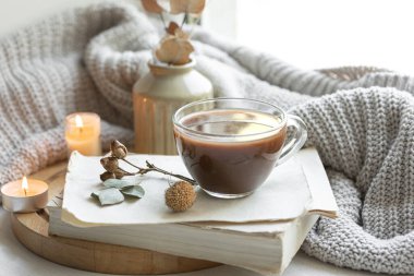 Bir fincan çay, kitaplar ve bulanık arka planda örülmüş bir element ile rahat ev kompozisyonu.