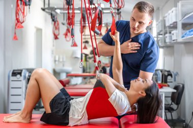 Kadın hastaya süspansiyon kayışları tedavisi uygulayan rehabilitasyon uzmanı, ağrısız dolaşım düzenini iyileştirmek için terapi egzersizleri, nöro-fonksiyon teknikleri..