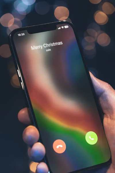 Incoming call screen from Merry Christmas in hands on a dark blurred background with bokeh.