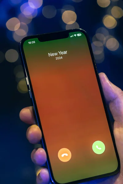 Incoming call screen from New Year 2024 in hands on a dark blurred background with bokeh.