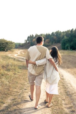 Bir erkek ve bir kadın bir tarlada kucaklaşarak yürür, arkadan bakar, mutlu bir ilişki kavramı, evlilikte aşk..